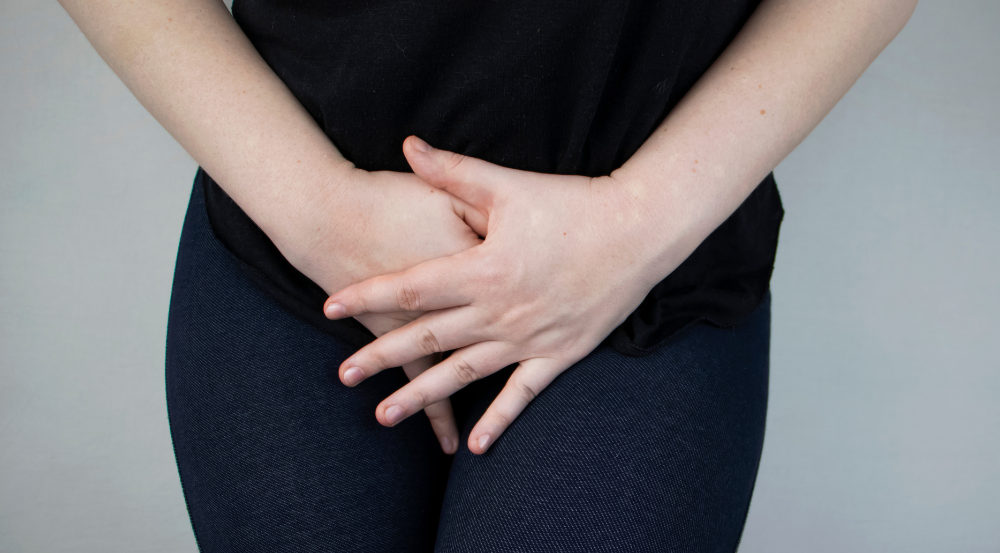 Person holding or covering their lower pelvic area with both hands